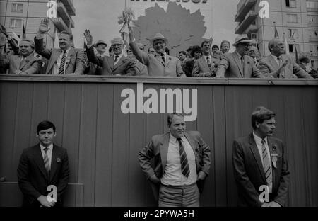 GDR, Berlin, 01.05.1987, 1. May rally 1987 on the Karl-Marx-Allee, tribune, Erich Honecker is handed flowers, left: Günter Schabowski, Willi Stoph (2nd from left), Horst Sindermann (2nd from right), Harry Tisch (1st from right), guards, personal security, [automated translation] Stock Photo