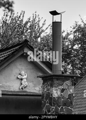 Black and white architectural detail of a house roof, chimney and small wall decoration, showing traditional exterior design, stonework and rustic res Stock Photo