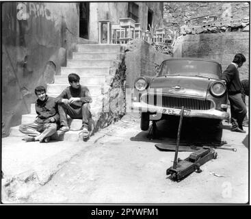 Istanbul (Turkey). Street scene: Men during lunch break (Beyoglu district) next to an old, jacked up Opel, car under repair. Black-and-white. Photo, 1994. Stock Photo