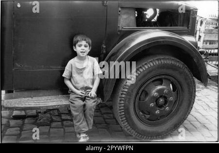 Ethnology: Turkey. Boy sitting on a truck running board next to large front wheel, on the street in Istanbul. Street scene, black and white. Photo, 1996. Stock Photo