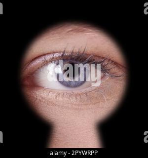 close-up of human female blue eye looking through keyhole Stock Photo