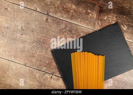 dry spaghetti pasta on a slate platter against a wood table top Stock Photo