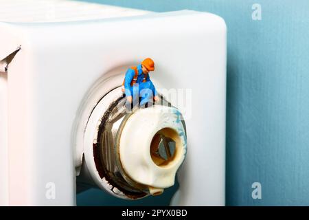 Conceptual image of a miniature figure workman inspecting the bleed valve on a central heating radiator Stock Photo