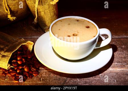 Coffee cup filled with coffee with sacks of raw roasted coffee beans Stock Photo