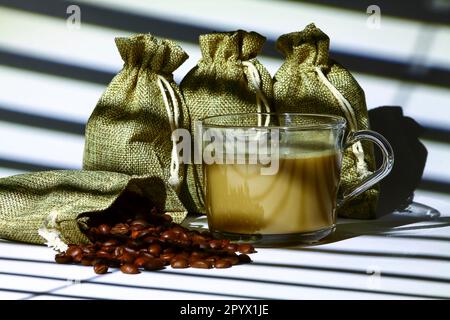 Shadow of a kitchen blind casting lines on to a cup of coffee and bags filled with raw coffee beans Stock Photo
