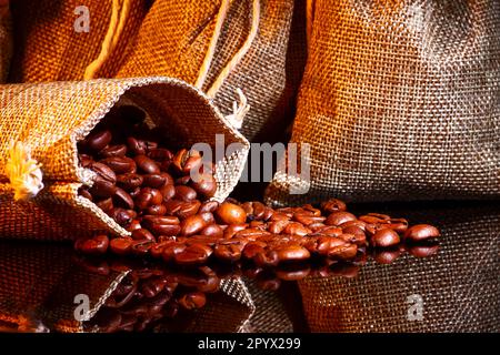 Bags filled with raw coffee beans spilling out on to black glass Stock Photo