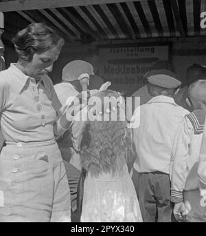 A woman holds an ice cream cone in her hand, right next to her is a little girl with a flower wreath in her hair (undated shot). Stock Photo