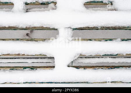 above view of snow-covered planks of wooden bench close up in city park on overcast winter day Stock Photo
