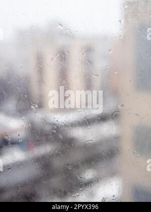 cold rain drops on surface of window glass in city apartment and view of city street on background Stock Photo