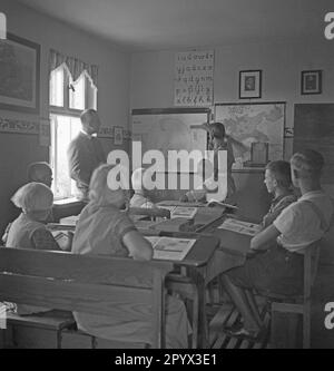 In a school on the Baltic Sea island of Ruden a teacher teaches students geography and local history. A student measures the scale with a ruler on a map showing the Baltic Sea coast and the island of Ruden and Usedom. Above a map of Germany hangs a portrait of Adolf Hitler. Stock Photo