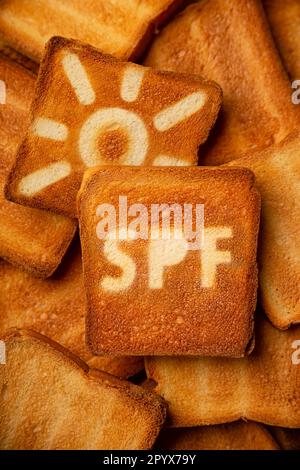 Concept of SPF cream and sun sign on toasted bread background. Stock Photo