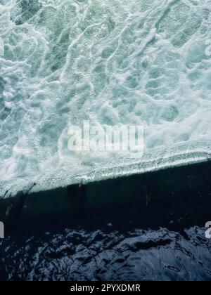 Abstract view of foamy turquoise water meeting dark sea surface, showing wave texture, natural patterns and dynamic ocean background. Stock Photo