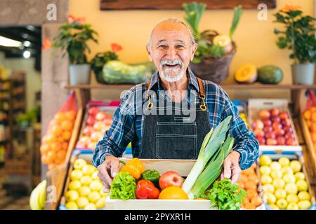 Senior greengrocer working at the market holding a box containing fresh fruits and vegetables - Food retail concept Stock Photo