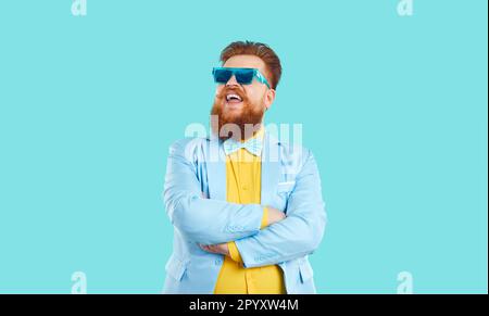 Cheerful bearded Caucasian man in funny sunglasses with arms crossed in front stands on studio Stock Photo