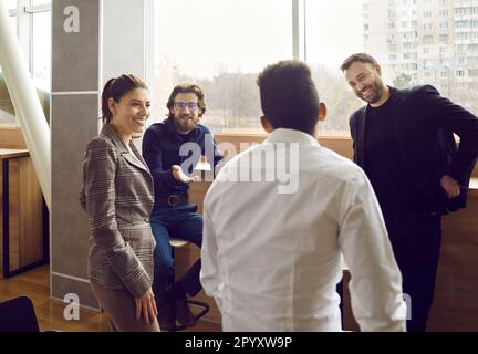 Collegues are talking in office during work break near the window, smiling and friendly people. Stock Photo