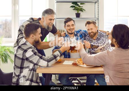Happy bearded male friends drinking beer and eating pizza at the party at home. Stock Photo