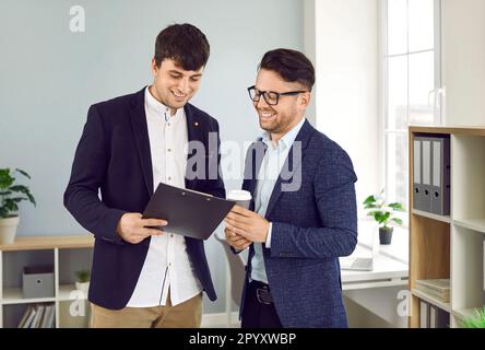 Two smiling male business colleagues in office reviewing and discussing paper documents. Stock Photo
