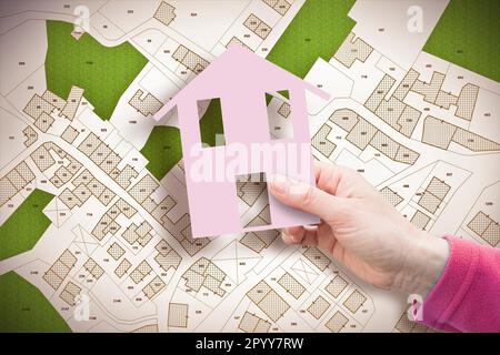 Vacant land for sale against an imaginary city map - vacant lot concept with hand holding a small house - NOTE: the map is totally invented and does n Stock Photo