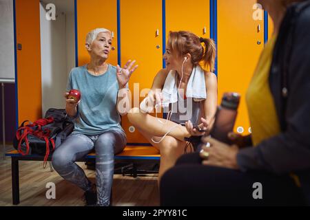 Women before workout in locker room having a conversation, senior woman with short hair talking to her friends. Togetherness, sport, active lifestyle Stock Photo