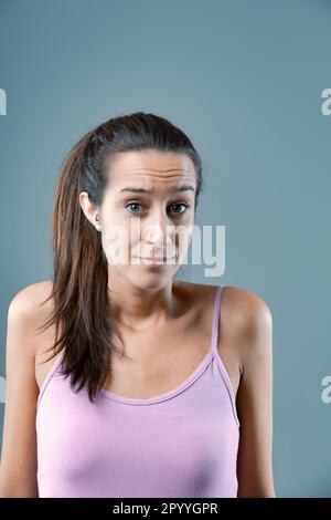 'What do I do now? I don't know.' Emotional portrait of young woman isolated on neutral background. Girl shows discomfort, doubt, every choice seems n Stock Photo