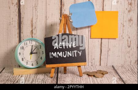 The text ACTIVE IMMUNITY is written in a yellow notebook that lies next to the stethoscope, medicine on a blue background. Medical concept Stock Photo
