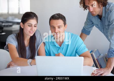 Three heads are better than one. three coworkers gathered around a laptop in the office. Stock Photo