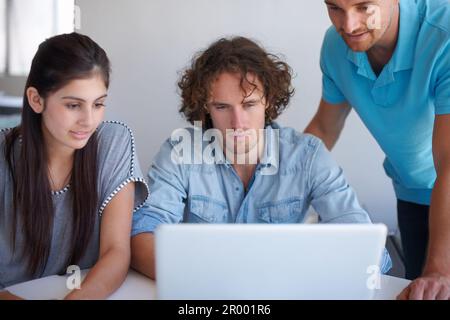Threes company. three coworkers gathered around a laptop in the office. Stock Photo