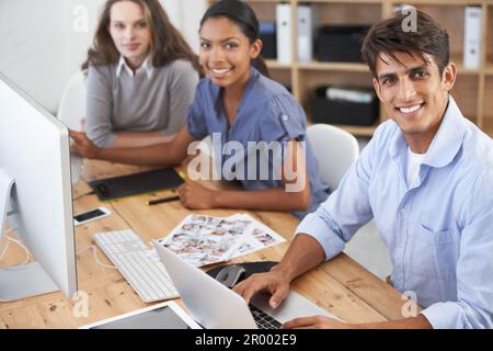 We come up with all the advertisements. three young colleagues working at a desk. Stock Photo