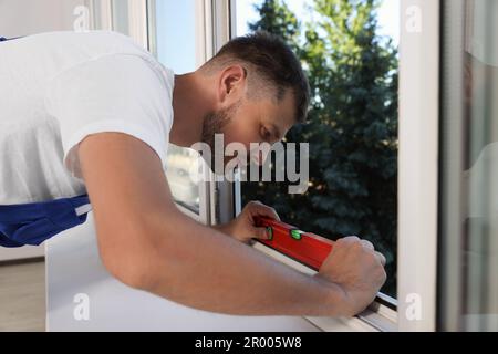 Worker using bubble level after plastic window installation indoors Stock Photo
