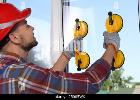 Worker using suction lifters during plastic window installation indoors Stock Photo