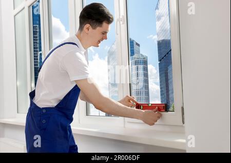 Worker using bubble level after plastic window installation indoors Stock Photo