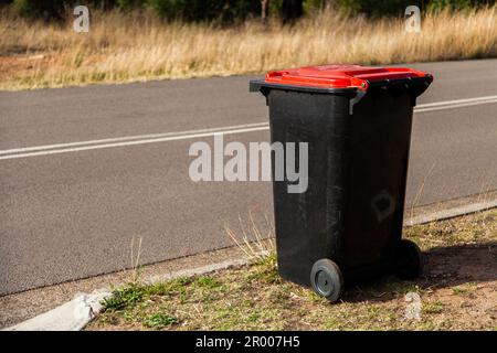 Red council garbage bin beside road awaiting collection Stock Photo