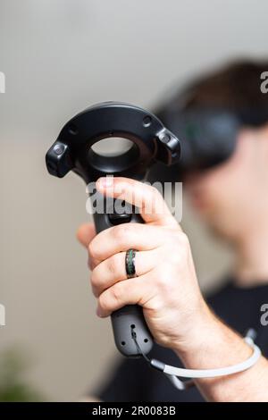 Focus on hand holding VR wand remote controller with young man playing virtual reality game Stock Photo