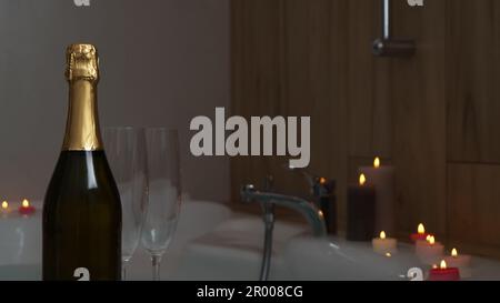 Bottle of champagne, glasses and burning candles near jacuzzi in bathroom, closeup Stock Photo