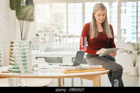 Leading businesswoman using a digital tablet. Mature boss using an online wireless device. Businesswoman in her creative agency. Senior creative Stock Photo