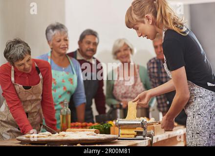 Food, senior cooking class and a woman teaching people in the kitchen of a home for meal preparation. Pasta maker, equipment and learning with mature Stock Photo