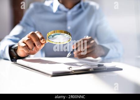 Close-up Of A Businessperson's Hand Holding Magnifying Glass Over Invoice At Workplace Stock Photo