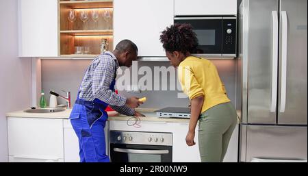 Male Repairman Installing Induction Cooker With Woman Standing In Kitchen Stock Photo