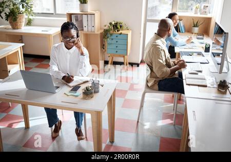 Working in a productive space. a young businesswoman using a headset and laptop in a modern office with her colleagues working beside her. Stock Photo