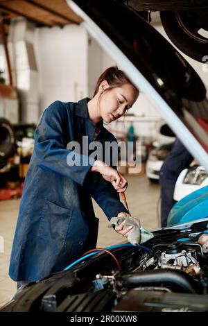 We do oil changes, tire rotation, air filter replacement and much more. a female mechanic holding a dipstick while checking a cars oil level. Stock Photo