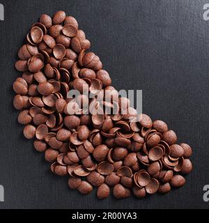 Directly above view of chocolate glazed shells on black stone background. Corn flakes for breakfast Stock Photo