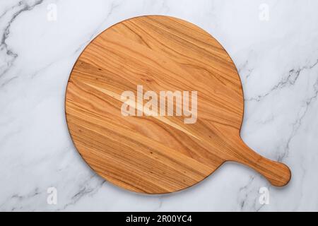 Round empty wooden charcuterie serving board with handle on a white or gray marble table, top view. Kitchenware, template with copy space. Flat lay de Stock Photo