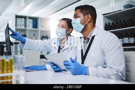 Hard work will get us the cure. two young researchers using digital devices in a laboratory. Stock Photo