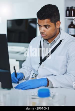 What does the data say. a young male researcher using a computer while taking notes in a laboratory. Stock Photo
