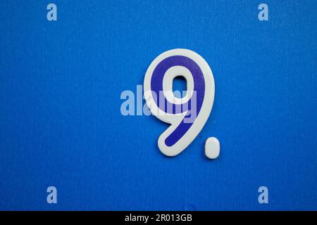 The number 9 in light blue and white color, placed on a blue background, photographed from above. Stock Photo
