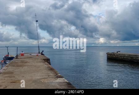 Two Local Fishermen waiting for another Man so that they can go out on their inshore Fishing Boat under dark Clouds from a small Port near to Librevil Stock Photo