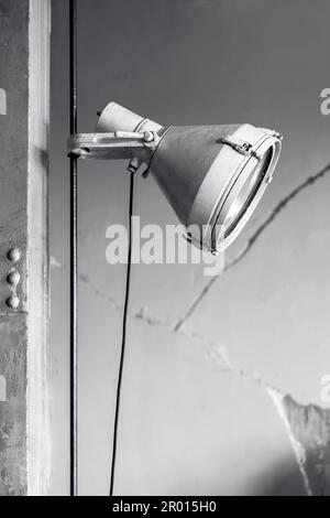 Minimal Industry style grey metallic lighting lamp on gray pillar and cracked wall background. Industrial building interior concept with copy space. Stock Photo