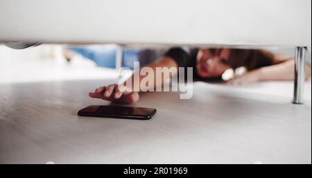 Girl Looking For Lost Mobile Phone Under Sofa Stock Photo