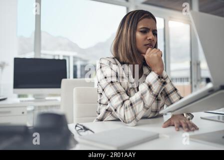 Difficult doesnt mean impossible. an attractive young businesswoman sitting alone in her office and looking confused while using her laptop. Stock Photo
