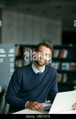 Traditional books have led us to the internet. Cropped portrait of a handsome young businessman sitting alone in a library and using his laptop. Stock Photo